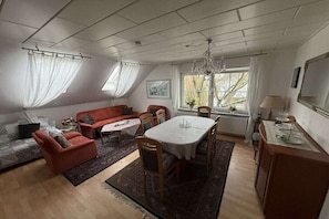 A living room with a sofa, chairs, a dining table, and a chandelier. - Holiday apartment with 2 bedrooms (Ostgroßefehn)