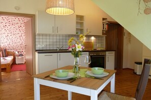 Ein Essbereich mit Tisch für zwei Personen, einer Blumenvase und einer Küche im Hintergrund.
