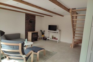 Ein Wohnzimmer mit einer Couch, Sesseln, einem Fernseher, einem Kamin und einer Holztreppe.