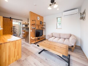 En moderne stue med sofa, fjernsyn, møbler af træ og et køkkenområde med mikrobølgeovn.