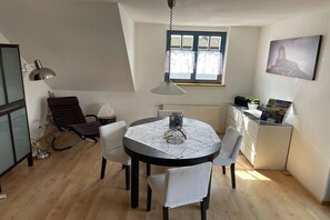 Ein Essbereich mit einem runden Tisch, Stühlen, einer Lampe, einer Heizung, einem Fenster und einem Wandbild.