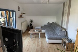 Ein Wohnzimmer mit Ecksofa, Couchtisch, Fernseher und Heizkörper.
