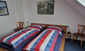 Une chambre à coucher avec un lit en bois, deux tables de chevet, une chaise et un tableau accroché au mur.