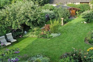 Ein gepflegter Garten mit Rasen, Sitzgelegenheit und einem kleinen Holzbau.
