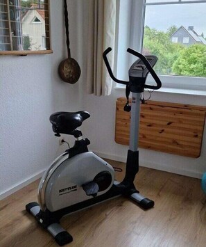 Ein stehendes Fitnessrad in einem Zimmer mit Fenster, Holzboden und Vorhang.