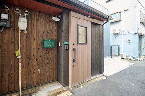 Une façade en bois avec une porte marron, une enseigne verte et un compteur d’électricité.