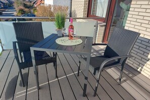 Ein Balkon mit Tisch, Stühlen, einer Weinflasche und einem Blumentopf.