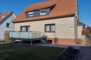 Ein zweigeschossiges Haus mit rotem Ziegeldach, einer überdachten Terrasse und einer Ziegel-Fassade.