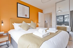 Ein Hotelzimmer mit einem großen Bett, einem Nachttisch mit Lampe, einem gerahmten Bild an der Wand und einem Fenster mit Blick.
