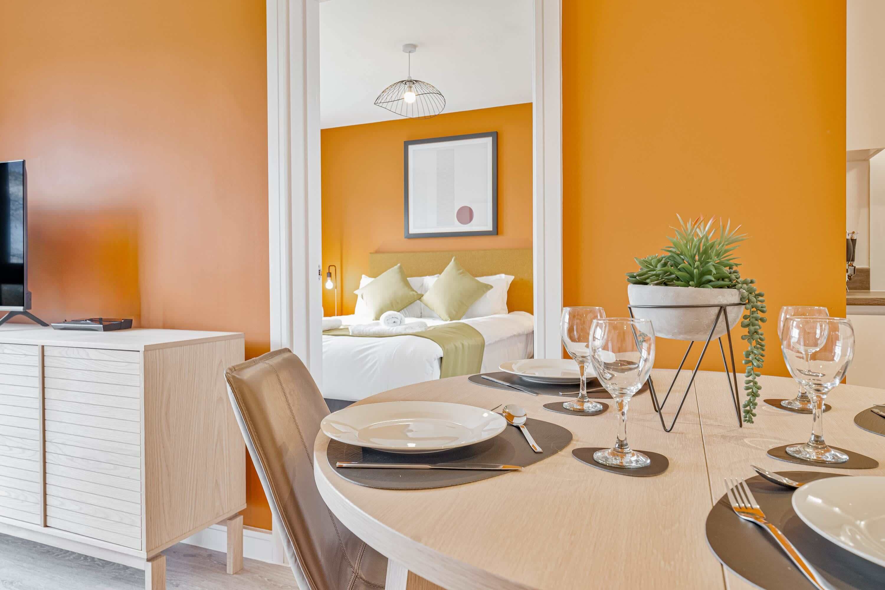 Habitación de hotel con comedor, una cama con almohadas, un televisor y una planta en maceta.