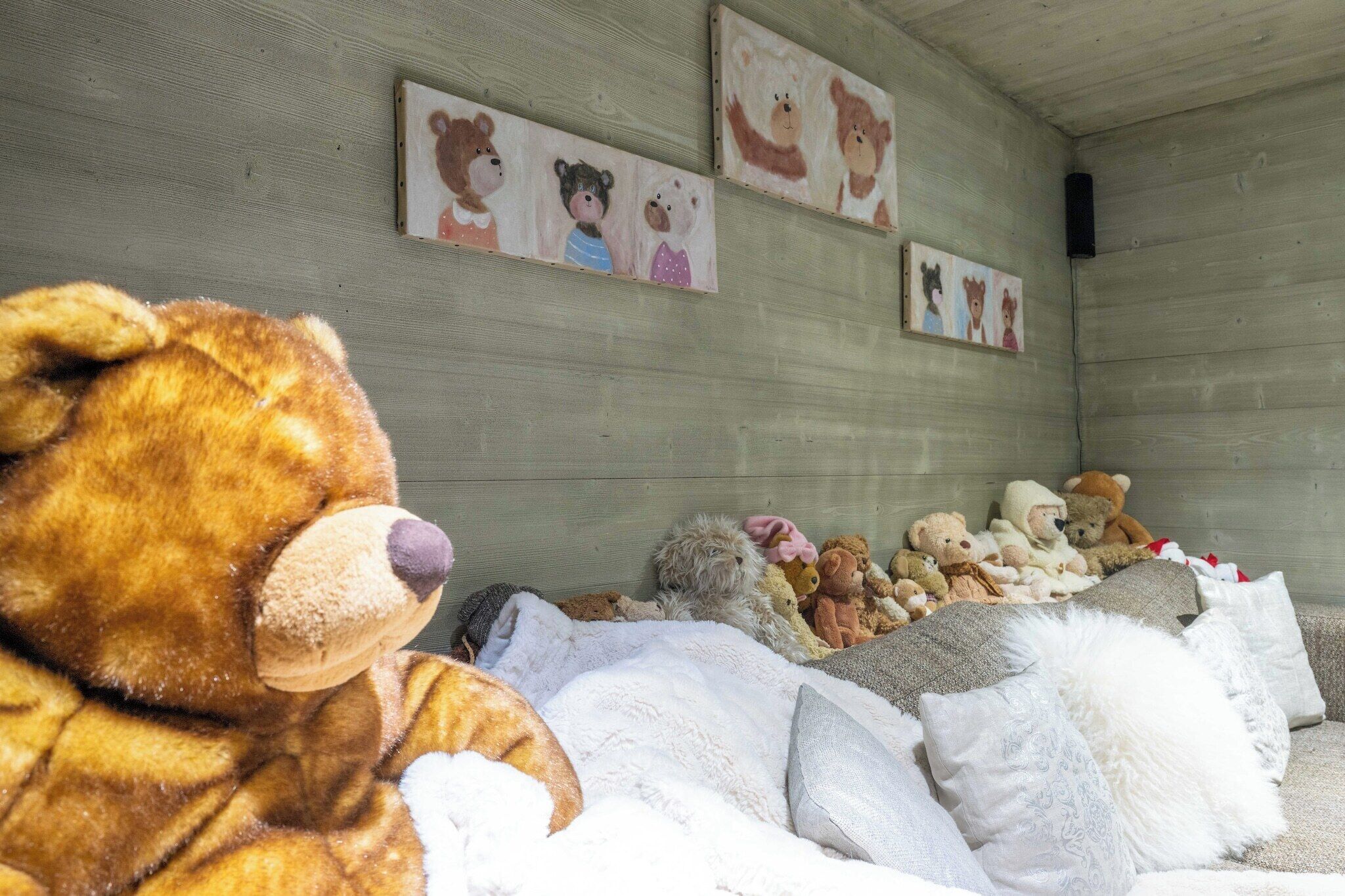 Una stanza con un grande orsetto di peluche, un letto con cuscini e decorazioni murali raffiguranti orsi.
