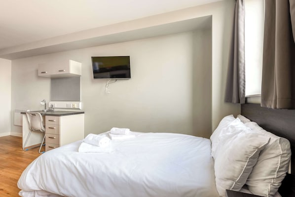 A bedroom with a bed, a desk, a chair, a TV, and a window.