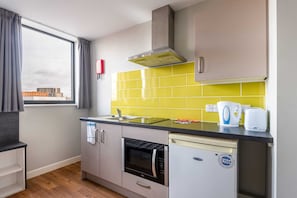 Une cuisine compacte dotée d’une fenêtre, d’un four encastré, d’un lave-vaisselle et d’un crédence jaune.