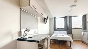 Quarto de hotel moderno com escrivaninha, cadeira, cama e janelas amplas.