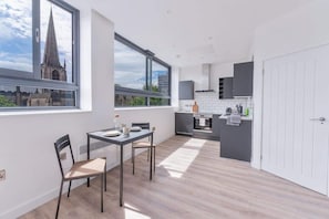 A modern kitchen with a view of a cathedral, a dining area with a table and chairs, and a white door. - Modern & Bright Central Sheffield Studio w Views (Sheffield)