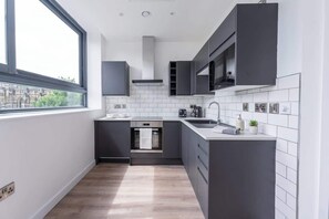 A modern kitchen with dark cabinets, a microwave, a stove, and a window providing a view of the city. - Modern & Bright Central Sheffield Studio w Views (Sheffield)