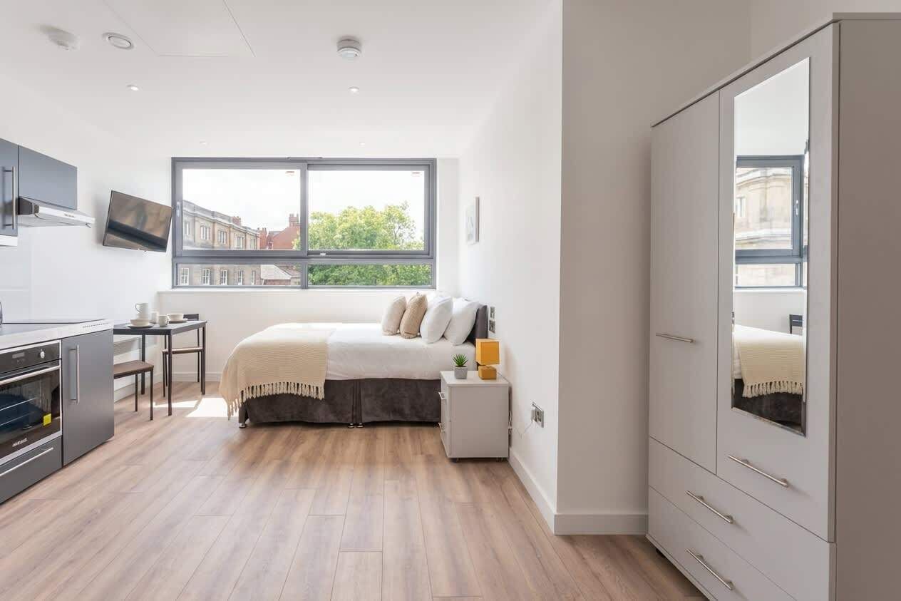 A modern bedroom with a bed, bedside table, wardrobe, and a window with a view of buildings.
