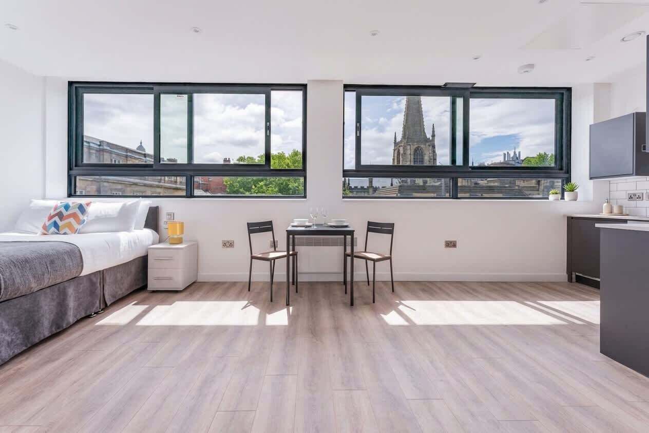 Une chambre moderne équipée d’un lit, d’une petite table, de deux chaises et de grandes fenêtres donnant sur la ville.