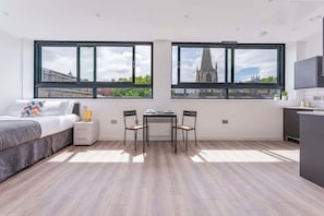 A modern room with a bed, a small table, two chairs, and large windows with a city view. - Modern & Bright Central Sheffield Studio w Views (Sheffield)