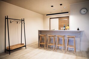 Une cuisine moderne avec un coin bar, des tabourets en bois, un panier suspendu et une horloge au mur.