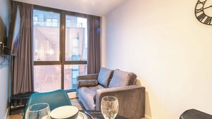 Ein modernes Wohnzimmer mit einer Couch, einem Esstisch mit Schüssel und Weinglas sowie einem großen Fenster mit Vorhängen.