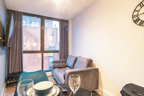 Ein modernes Wohnzimmer mit einer Couch, einem Esstisch mit Schüssel und Weinglas sowie einem großen Fenster mit Vorhängen.