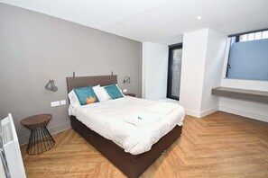 Ein modernes Schlafzimmer mit einem großen Bett, Nachttischlampen, einem kleinen runden Tisch und einem Fenster mit Jalousien.