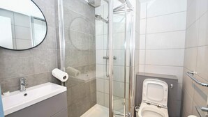 Un baño moderno con cabina de ducha de vidrio, lavamanos e inodoro.