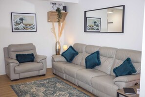 Ein Wohnzimmer mit einem beigefarbenen Sofa, einem Sessel, einem Teppich und zwei gerahmten Kunstwerken.