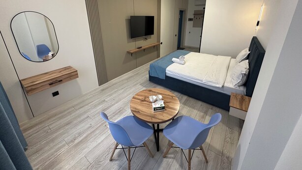 A modern hotel room with a bed, a TV, a small table with chairs, a mirror, and a wooden side table. - Dream Hotel Mayram (Kok-Jar)