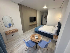 A modern hotel room with a bed, bedside table, TV, and a dining area with chairs. - Dream Hotel Mayram (Kok-Jar)
