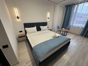 Une chambre dâhĂŽtel moderne avec un grand lit, des tables de chevet, une petite table ronde avec des chaises et une fenĂȘtre avec des rideaux.