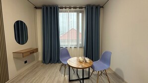 A room with a round wooden table, two blue chairs, a wooden bench, a round mirror, and a window with curtains. - Dream Hotel Mayram (Kok-Jar)