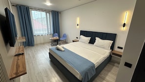 Une chambre dâhĂŽtel moderne, dotĂ©e dâun grand lit, dâun bureau avec une chaise, dâune petite table et dâune fenĂȘtre avec des rideaux.