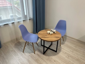 A room with a round wooden table, two blue chairs, and a window with curtains. - Dream Hotel Mayram (Kok-Jar)