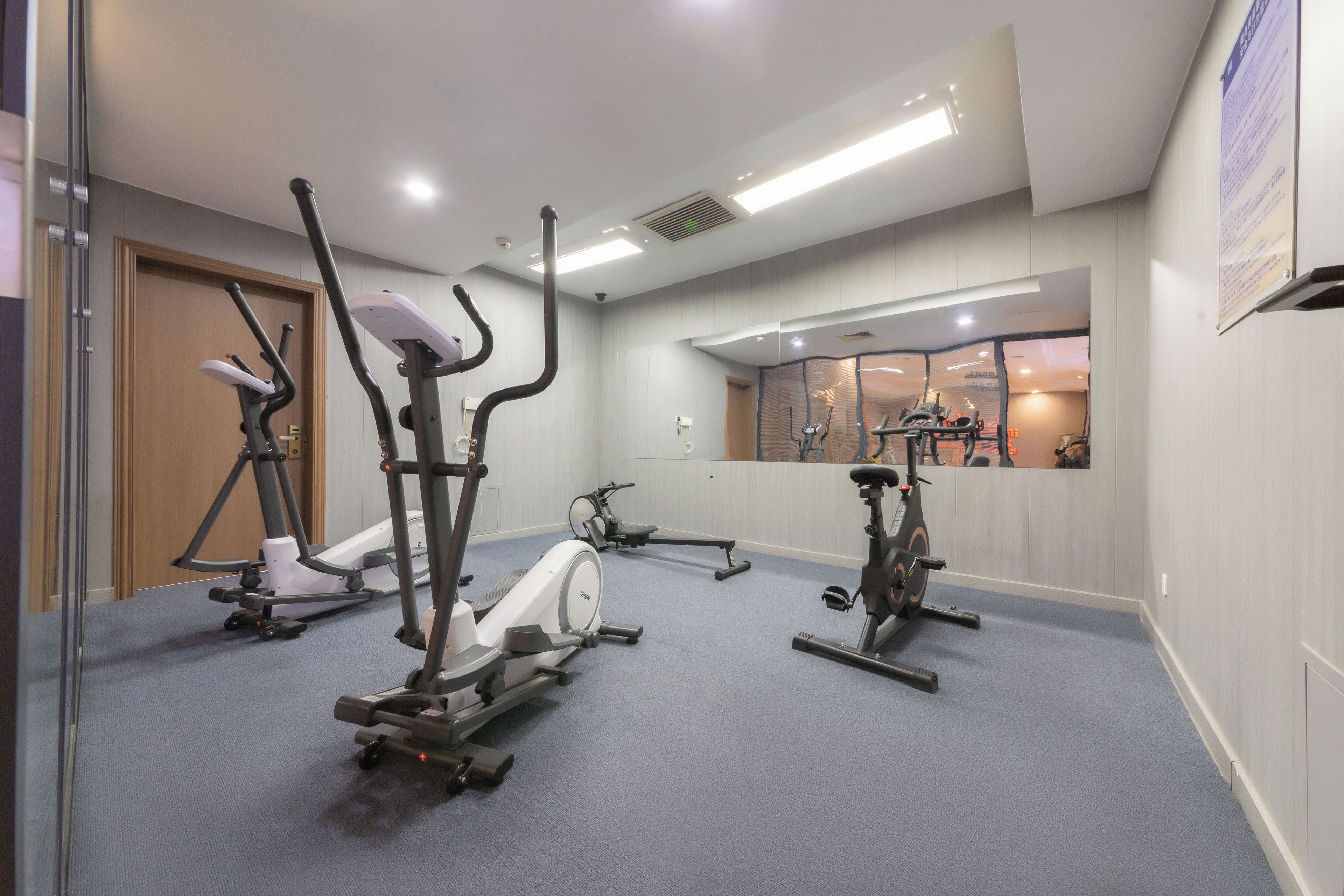 Un gimnasio con diversas máquinas de ejercicio, un espejo y un ventanal con vistas al exterior.