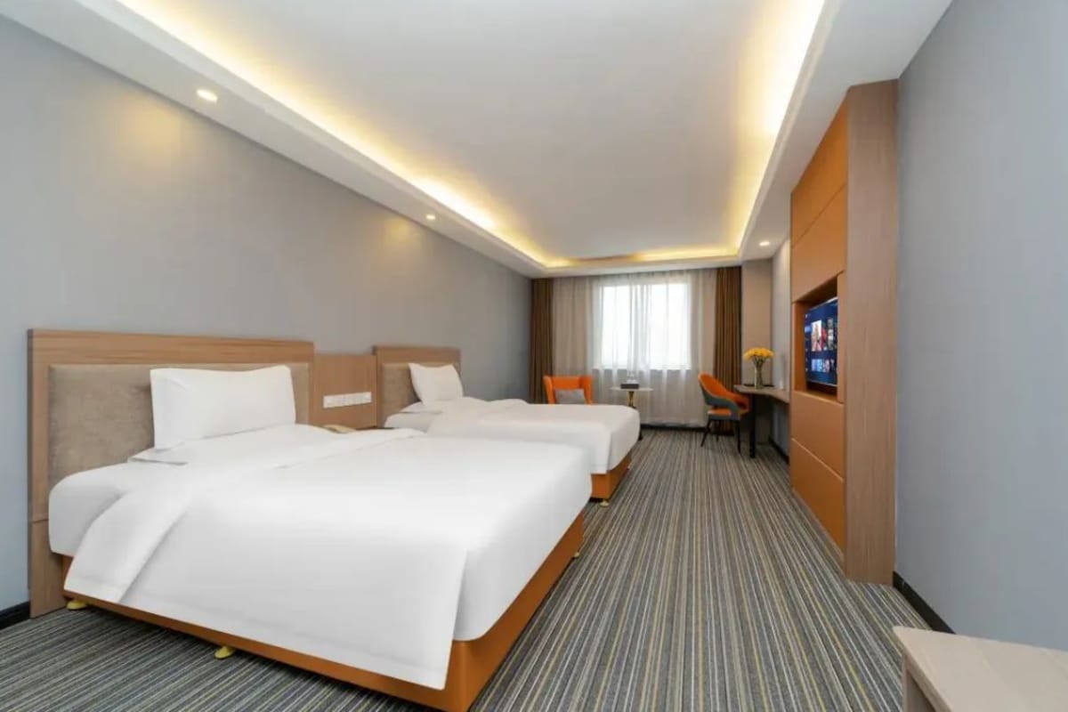 A hotel room with two beds, a desk, and a television.