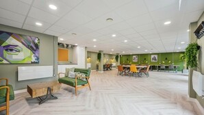 En modern inredning med en grön vägg, ett träbord som används som soffbord och en matplats med stolar och ett bord.