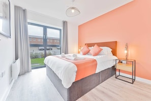 Ein modernes Hotelzimmer mit einem großen Bett, einem Nachttisch, Blick ins Freie und einem Vorhangfenster.