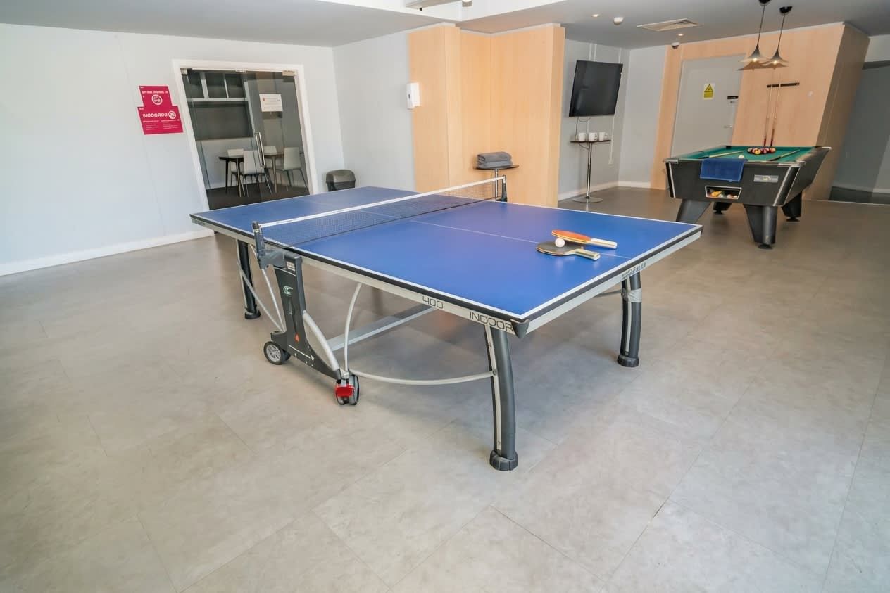 A ping pong table in a room with a pool table and a television.