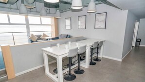 Een moderne keuken met een wit aanrecht, barstoelen, hanglampen en uitzicht door grote ramen.