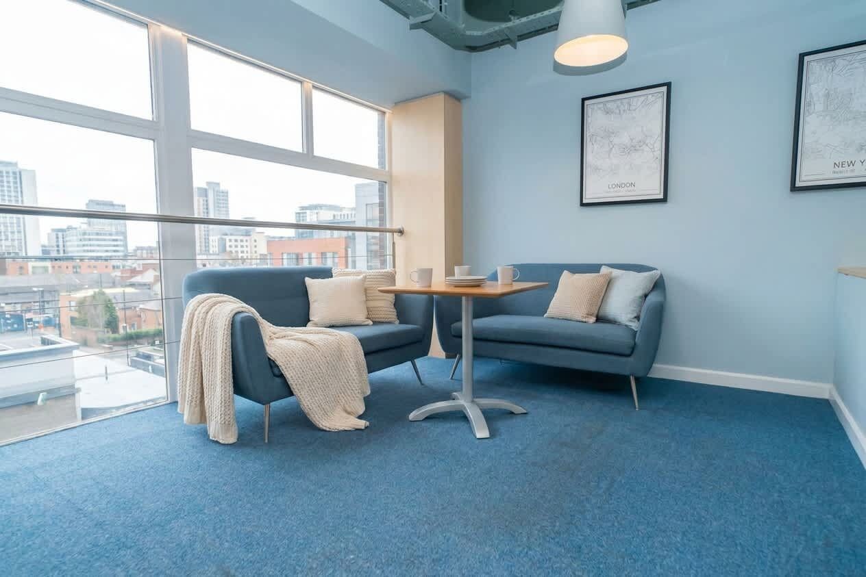Un espacio de oficina moderno con alfombra azul, un sofá gris, una pequeña mesa y cuadros con vistas a la ciudad en la pared.