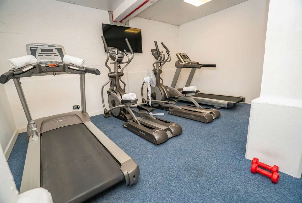 A fitness room with treadmills, a TV, and red dumbbells.