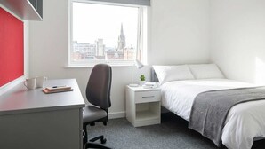 Een hotelkamer met een bureau, stoel, bed, nachtkastje en een raam met uitzicht op de stad.