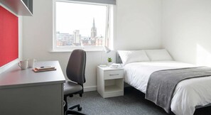 A hotel room with a desk, chair, bed, nightstand, and a window with a city view. - Central Coventry Budget Studio w Gym & Games Room (Coventry)
