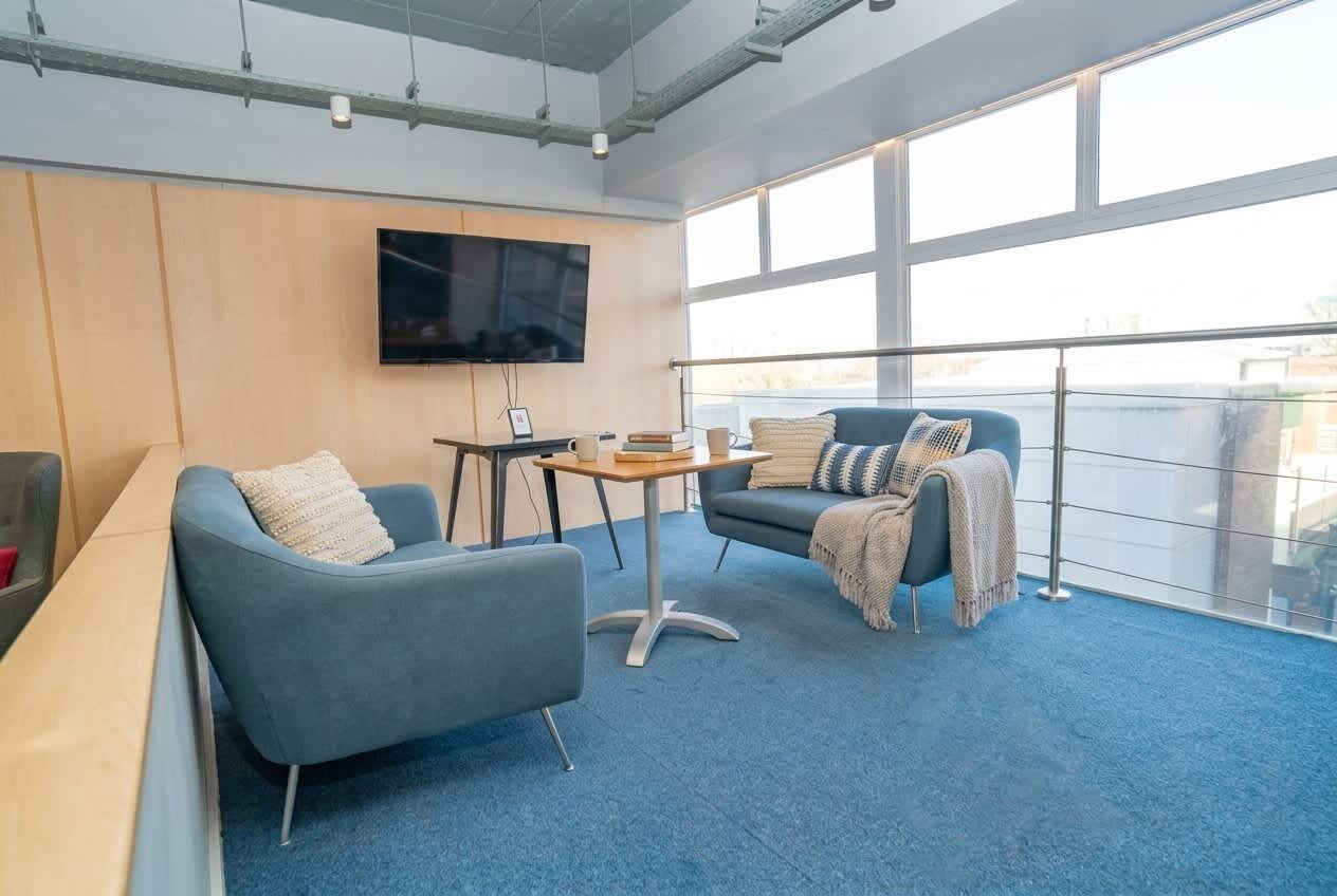 Eine moderne Lounge mit Flachbildfernseher, zwei Sofas mit Kissen, einem kleinen runden Tisch und einem großen Fenster mit Aussicht.