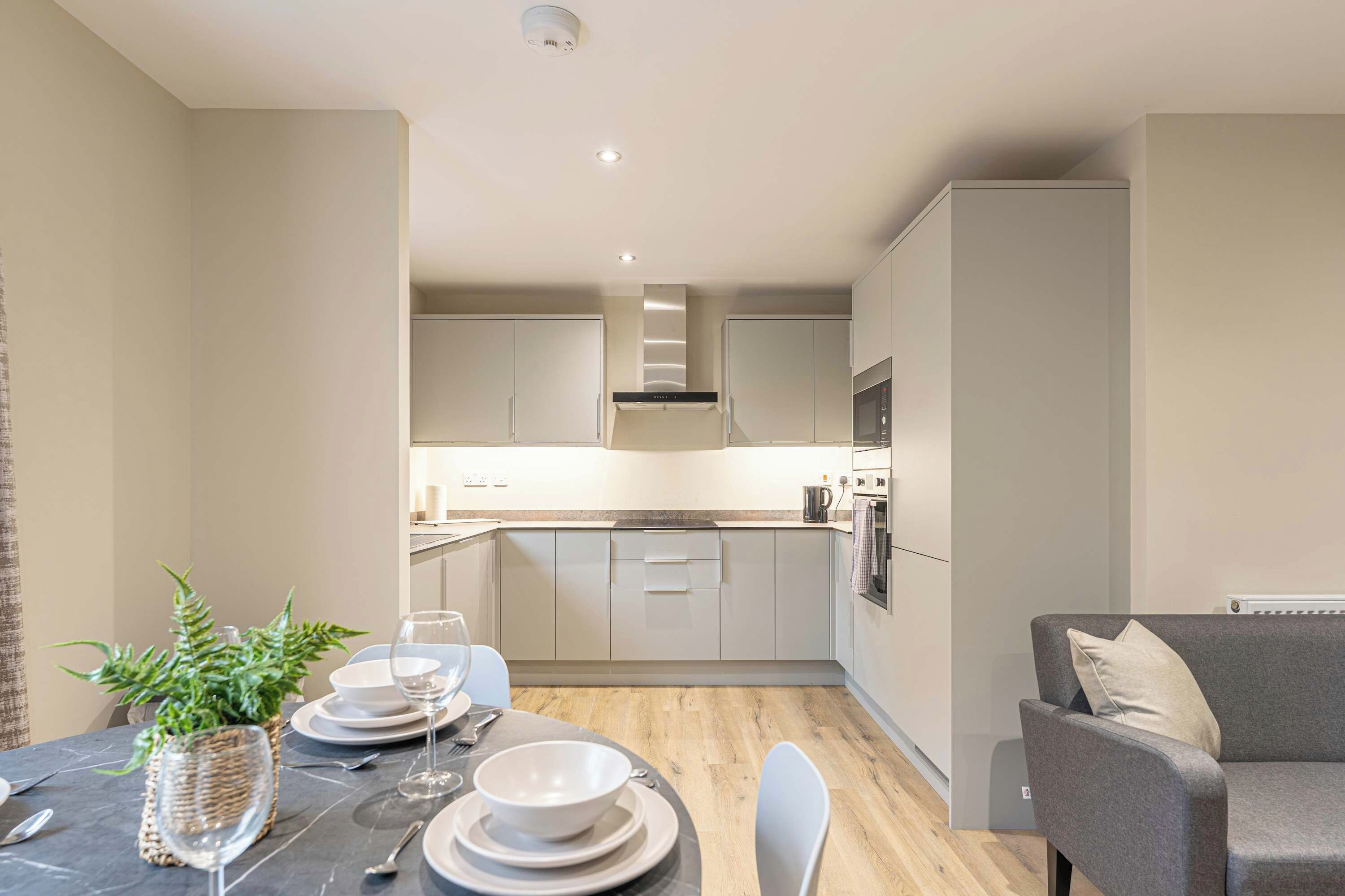A modern kitchen with white cabinets, a built-in oven, and a dining area with a table set for two.