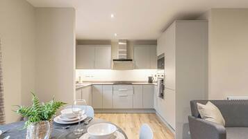 A modern kitchen with white cabinets, a built-in oven, and a dining area with a table set for two.