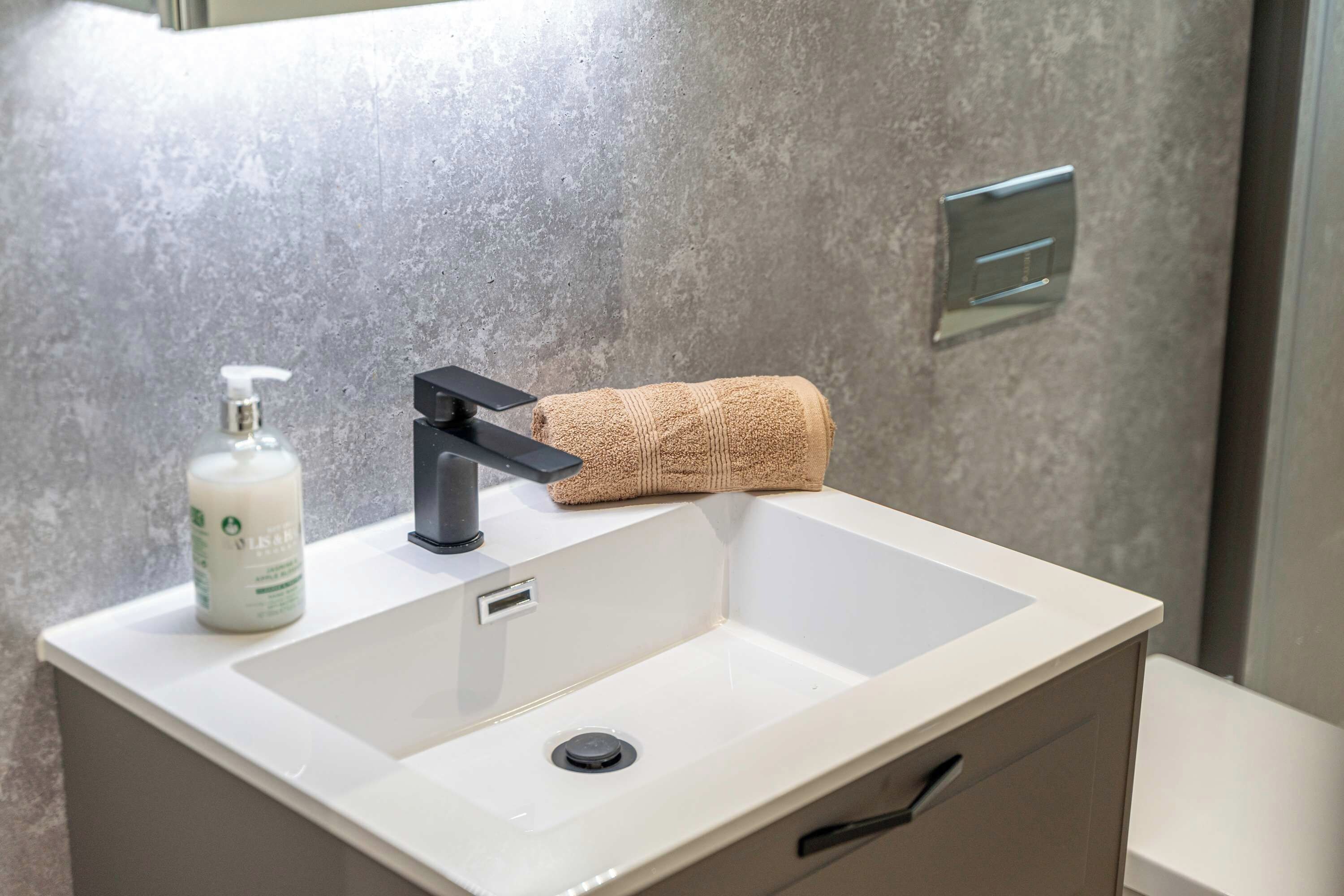 A bathroom sink with a modern faucet, a bottle of hand soap, and a rolled-up towel.