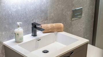 A bathroom sink with a modern faucet, a bottle of hand soap, and a rolled-up towel.